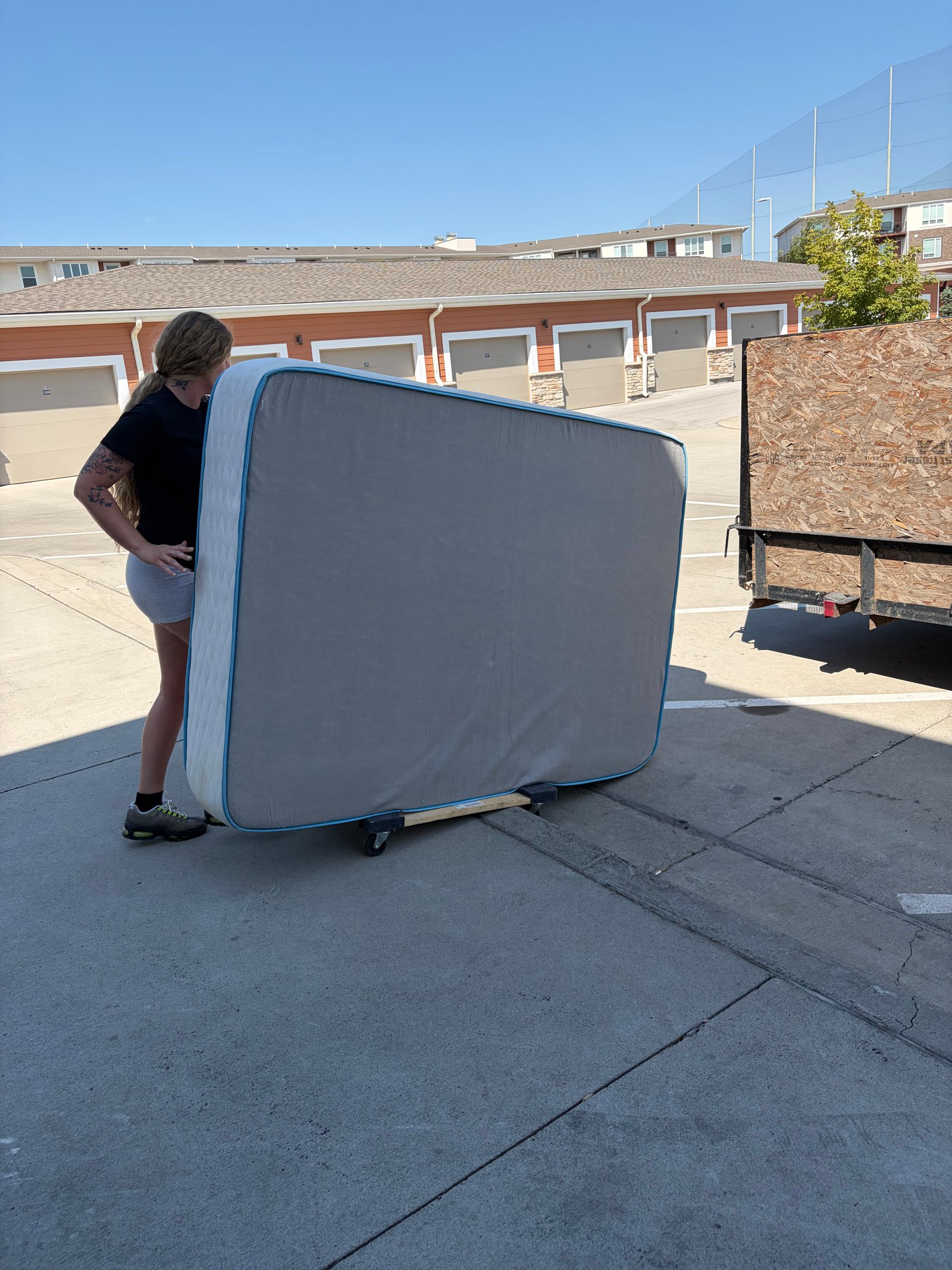 A worker moving a mattress on a dolly beside a trailer